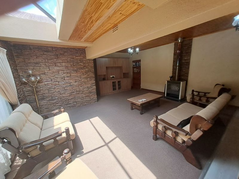 Spacious living room featuring a stone accent wall, wood-burning fireplace, built-in cabinetry, and a large skylight providing ample natural light.