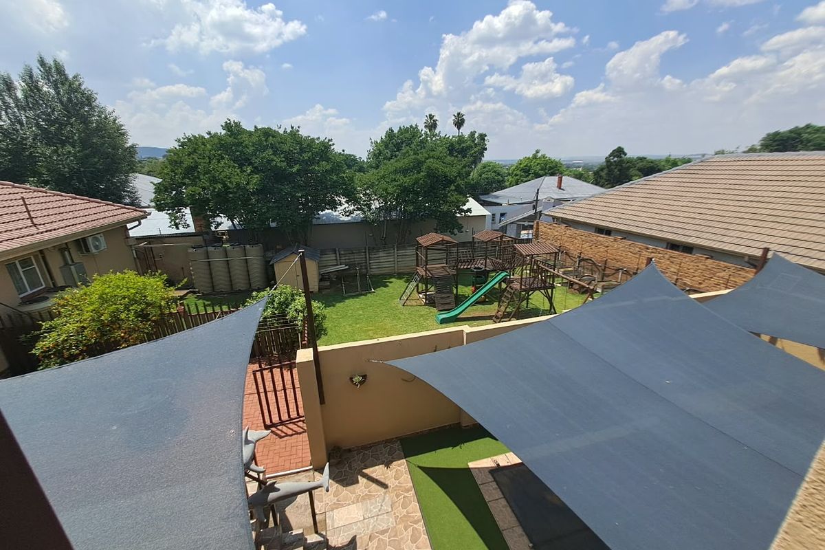Elevated view of a rear garden featuring a paved patio area with shade sails, artificial turf, and perimeter walling.