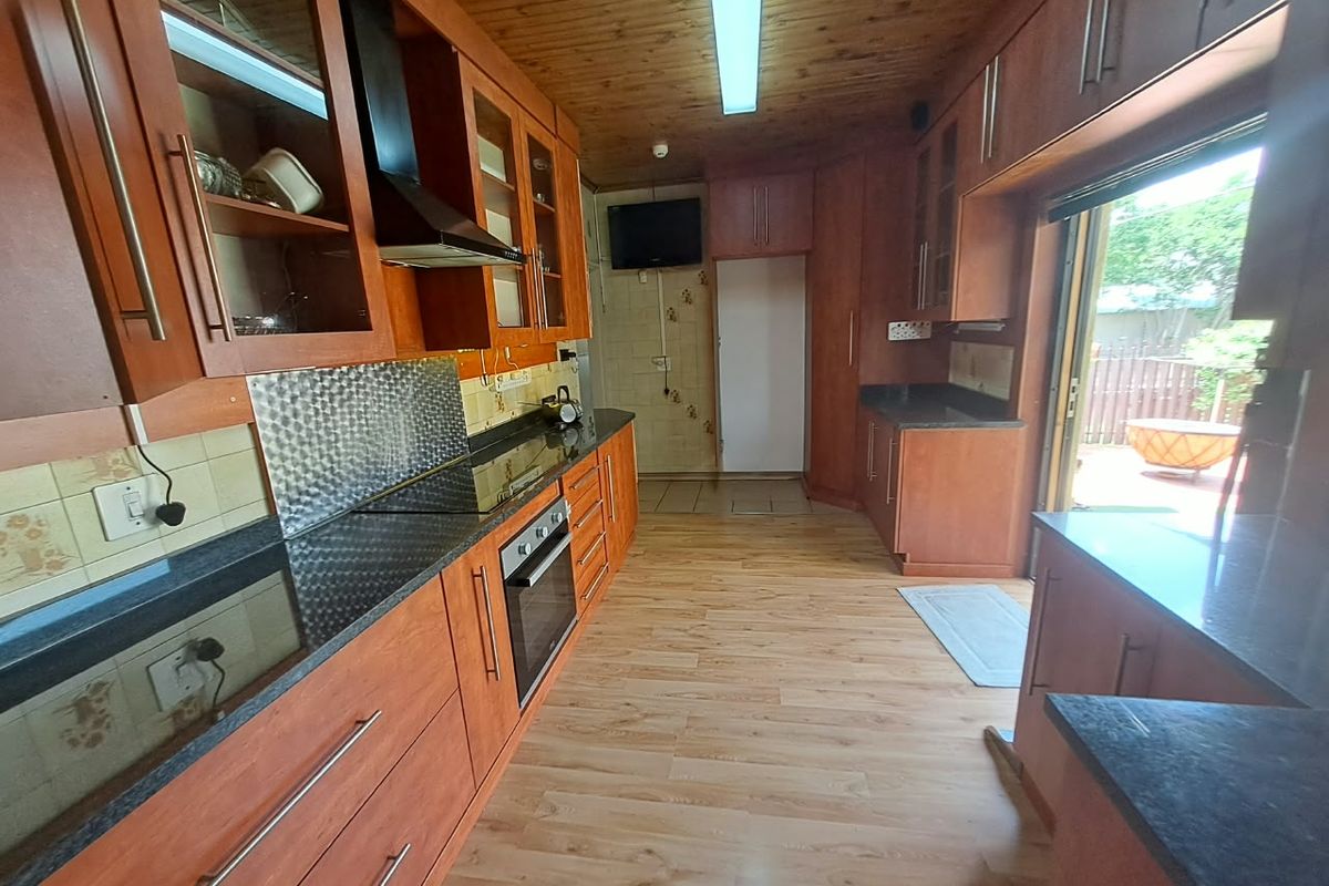 A functional kitchen featuring wooden cabinetry, granite countertops, built-in oven and hob, with direct access to an outdoor patio area.