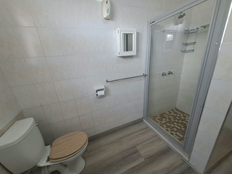 A functional bathroom featuring a glass-enclosed shower, toilet, and tiled wall finishes with a neutral aesthetic.
