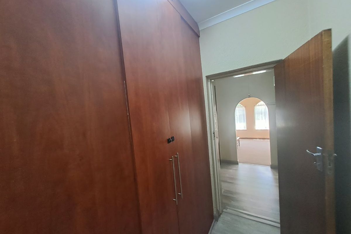 A bedroom featuring built-in wooden cupboards, laminate flooring, and coving, with a doorway leading to an adjacent living area.