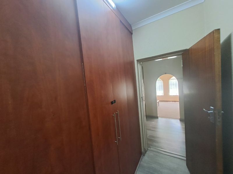 A bedroom featuring built-in wooden cupboards, laminate flooring, and coving, with a doorway leading to an adjacent living area.