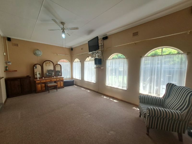 Spacious living room featuring arched windows, carpeted flooring, and a ceiling fan, offering a versatile layout with neutral wall finishes.