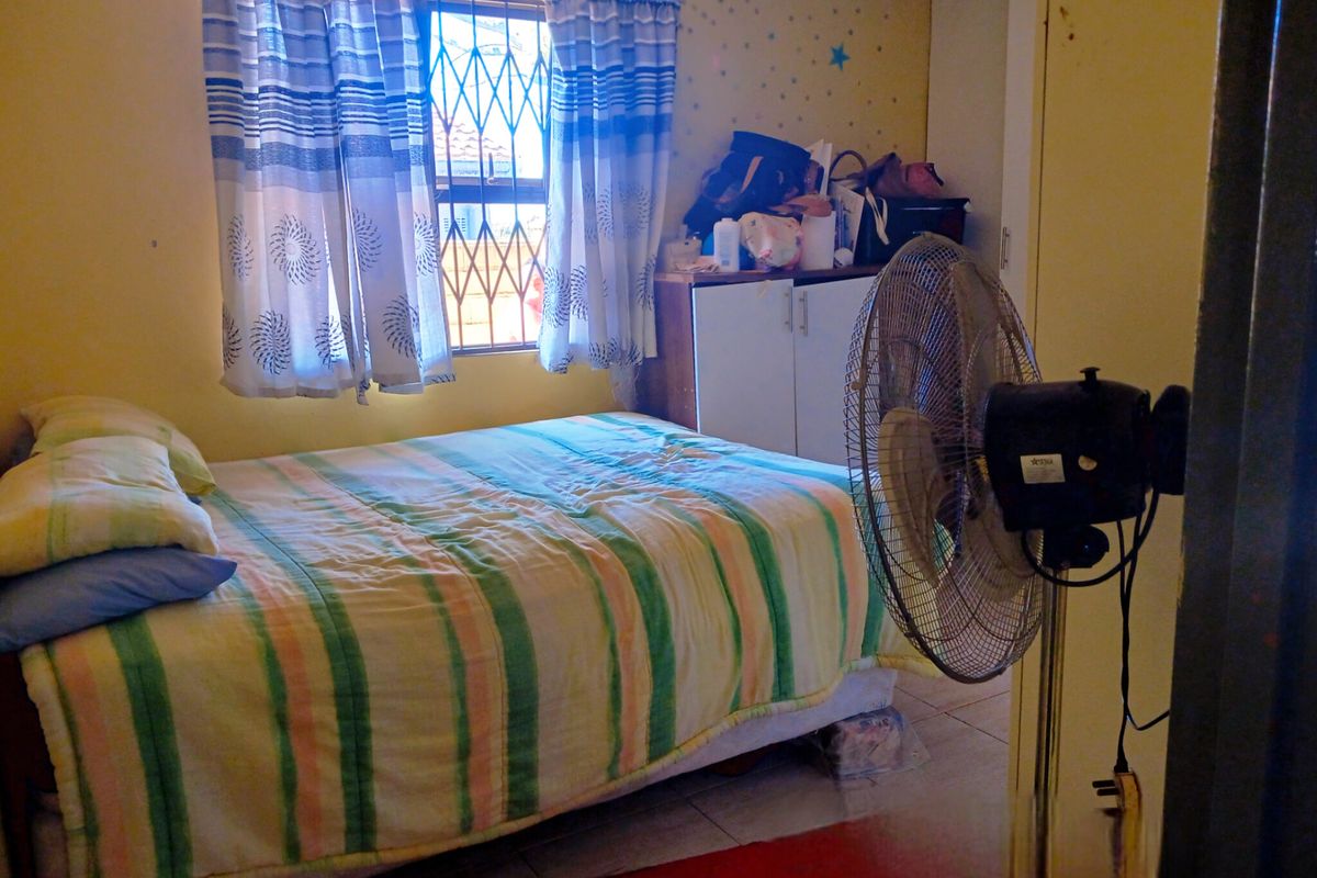 A bedroom featuring tiled flooring, a built-in cupboard, and a window fitted with a security gate.