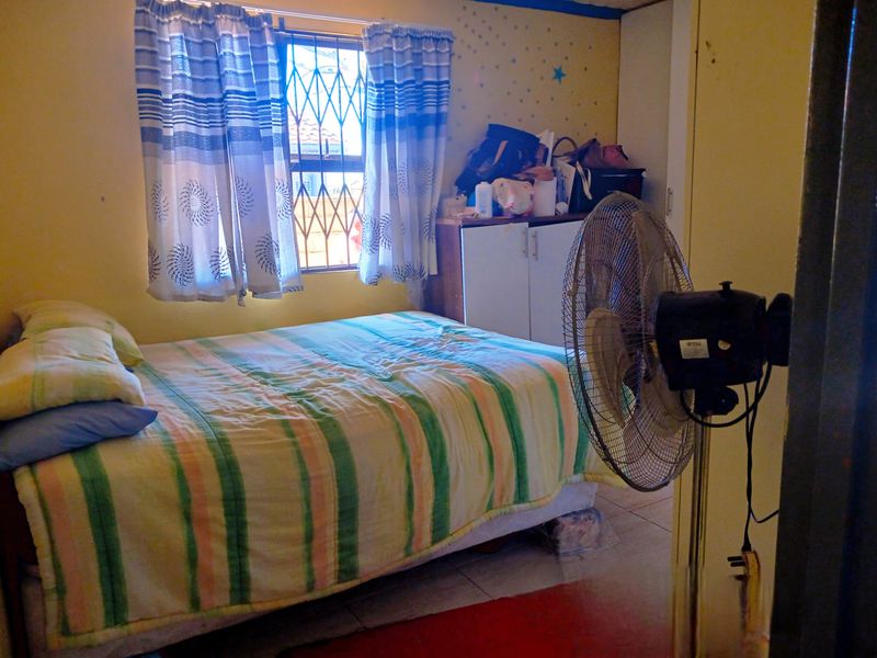A bedroom featuring tiled flooring, a built-in cupboard, and a window fitted with a security gate.