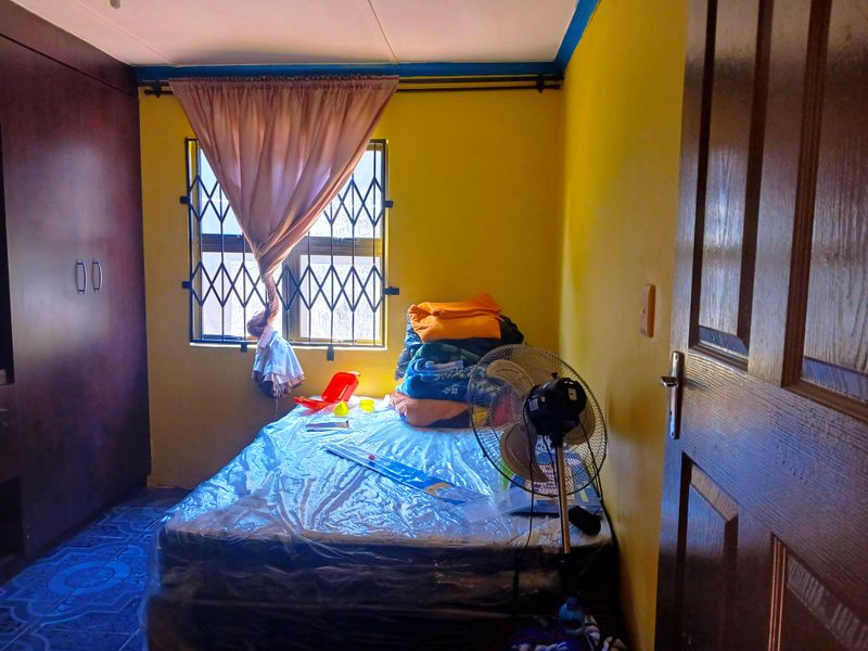 A bedroom featuring built-in wardrobes, tiled flooring, and a window fitted with a security gate.