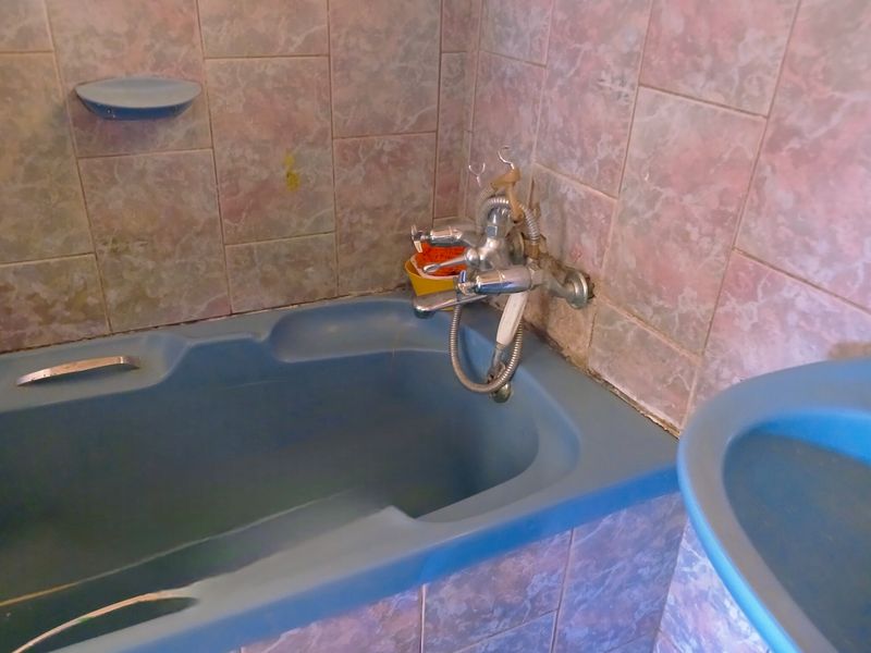 A dated bathroom featuring a blue bathtub and matching wall tiles, requiring modernization of fixtures and finishes.