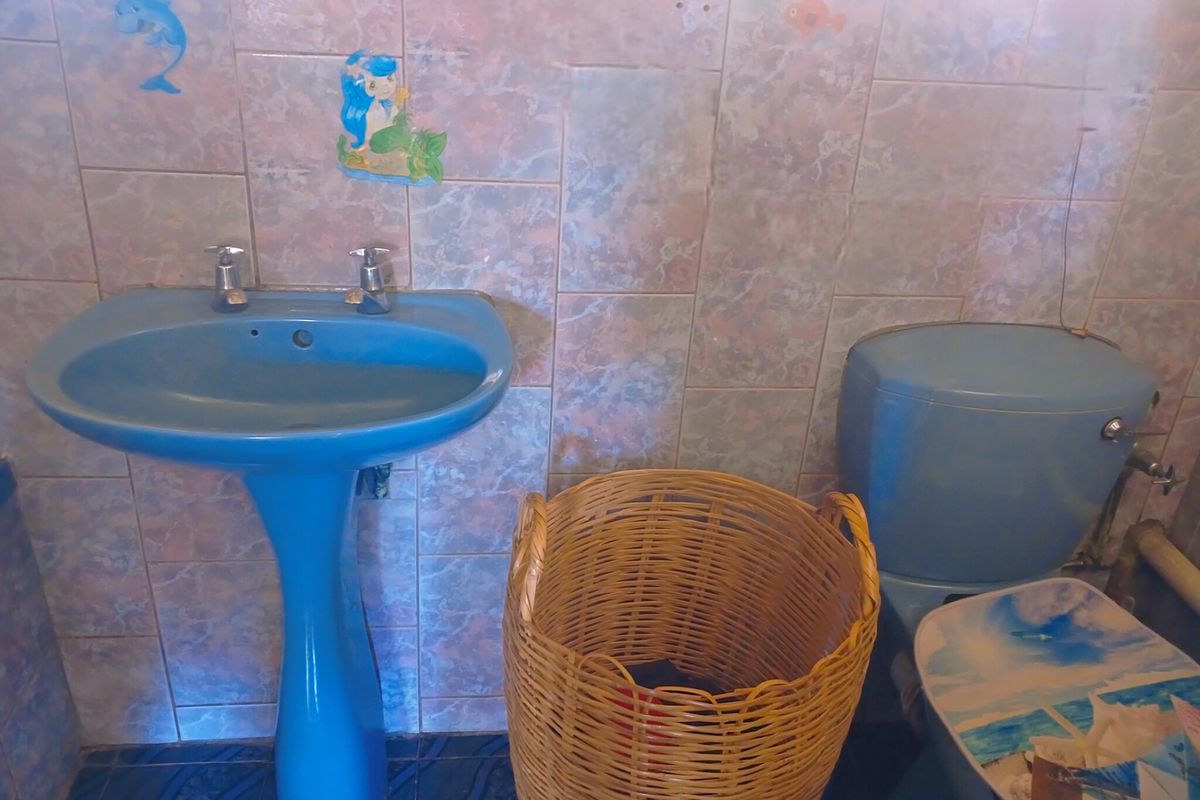 A dated bathroom featuring blue sanitaryware, including a pedestal basin and toilet, finished with patterned wall and floor tiles.
