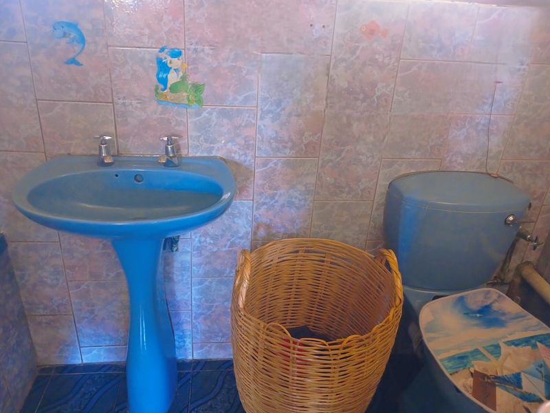 A dated bathroom featuring blue sanitaryware, including a pedestal basin and toilet, finished with patterned wall and floor tiles.