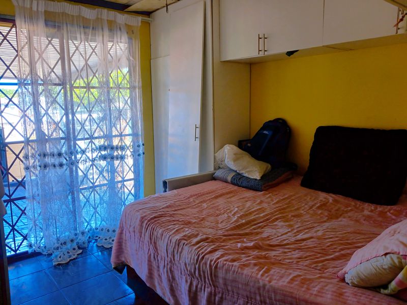 A bedroom featuring built-in cupboards, overhead storage, tiled flooring, and a security gate leading to an outdoor area.