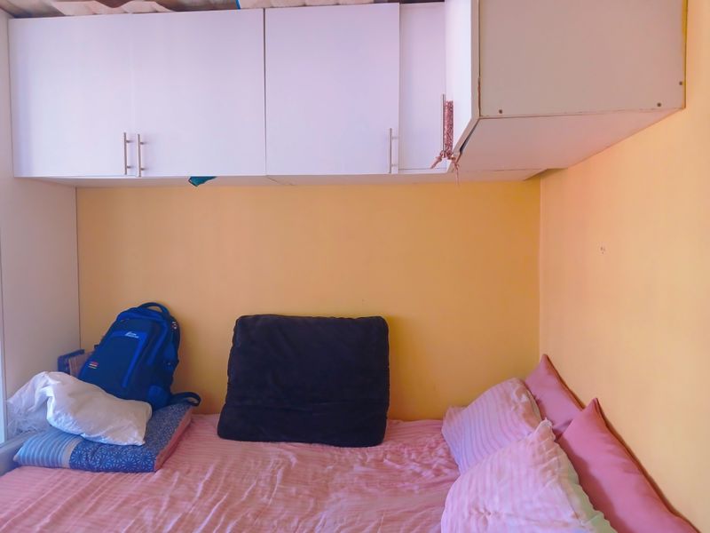 A compact bedroom featuring built-in overhead storage cabinetry and yellow wall finishes.