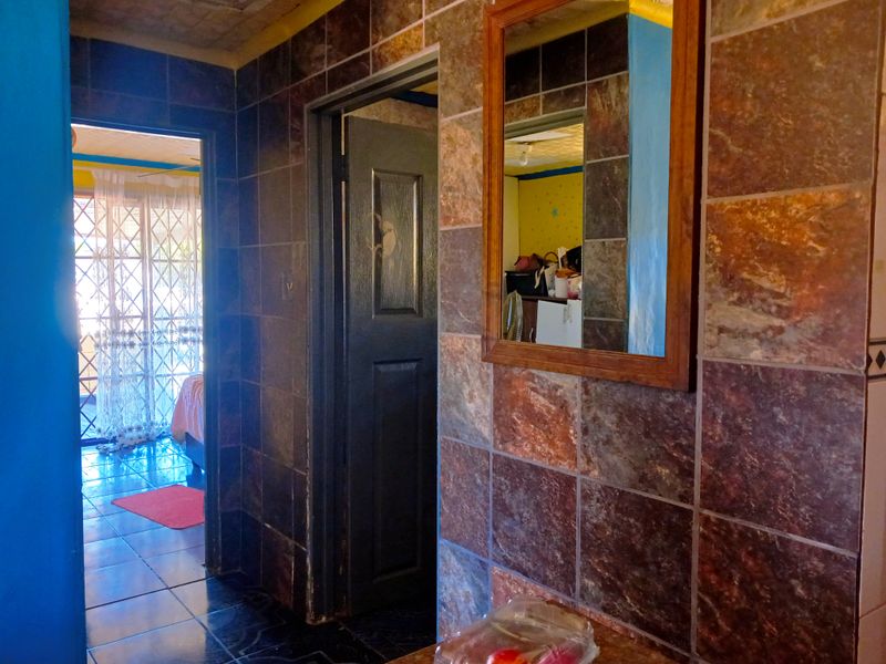 A hallway featuring dark tiled walls and flooring, with an integrated wall mirror and access to adjacent rooms.