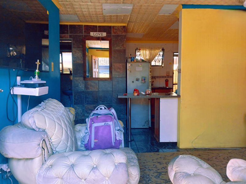 Open plan living and kitchen area featuring tiled flooring, a breakfast bar, and a tiled splashback, offering a functional layout with potential for modernization.