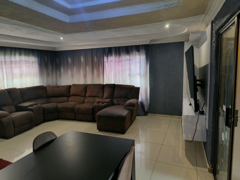 Spacious living room featuring tiled flooring, a recessed ceiling design, and a wall-mounted television setup with access to an adjacent area via a sliding door.