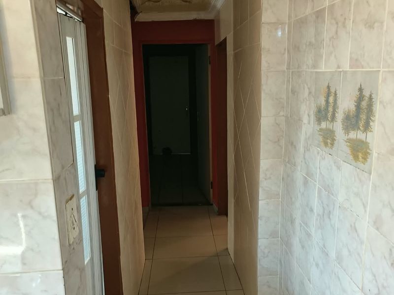 A narrow hallway featuring tiled walls and flooring, with decorative ceiling molding and a central light fixture.