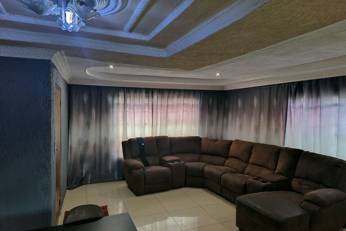 A spacious living room featuring tiled flooring, an ornate ceiling rose with decorative molding, and recessed lighting, creating a comfortable and well-defined living area.