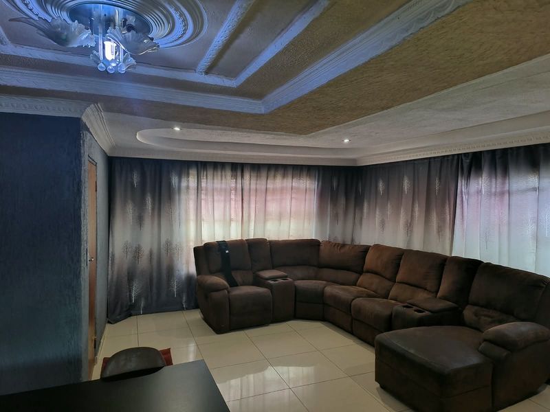 A spacious living room featuring tiled flooring, an ornate ceiling rose with decorative molding, and recessed lighting, creating a comfortable and well-defined living area.