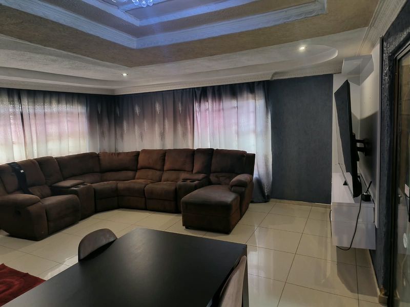 Spacious living room featuring a decorative recessed tray ceiling with cove lighting and neutral ceramic floor tiles throughout.