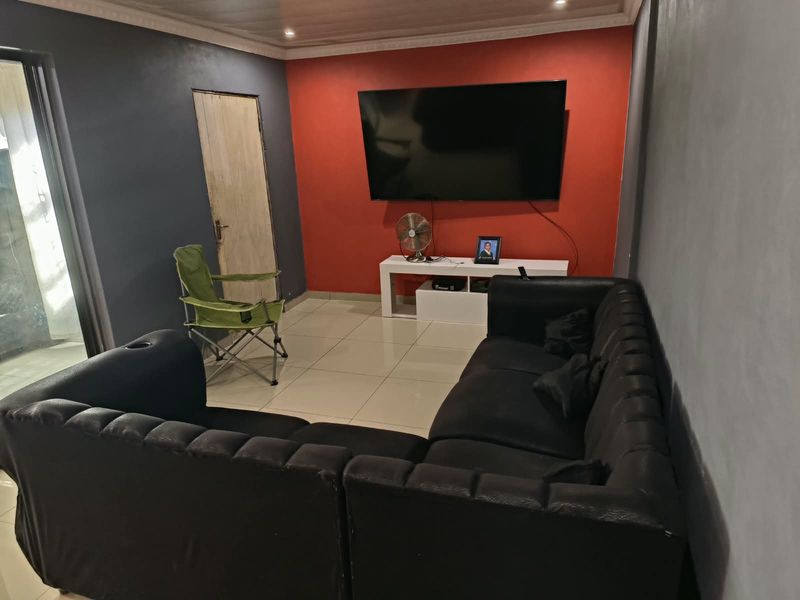 Living room featuring tiled flooring and a coved ceiling, currently utilized as a media space with a bold red accent wall.