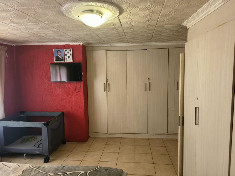 Bedroom featuring built-in cupboards, tiled flooring, and textured ceiling tiles. The space offers functional storage and requires cosmetic updates to modernize the finishes.