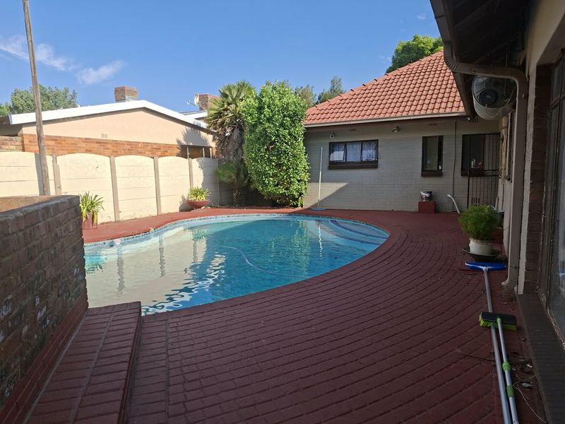 A private backyard featuring a swimming pool surrounded by a red-painted brick patio and enclosed by a precast concrete boundary wall.