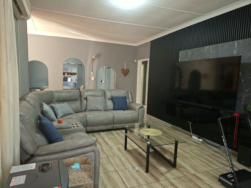 A comfortable living room featuring tiled flooring, a modern slatted feature wall, and distinctive archway openings leading to adjacent spaces.