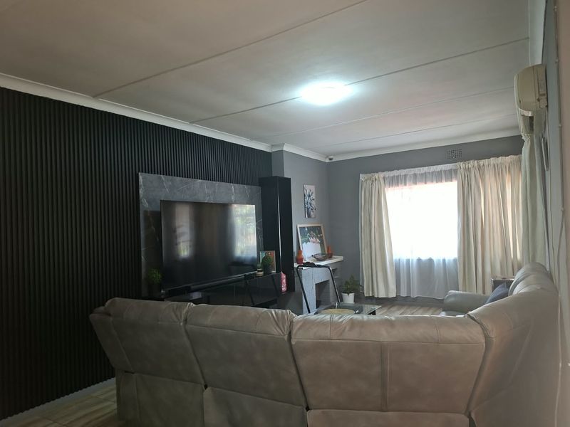 A comfortable living room featuring a modern slatted accent wall, marble-look paneling, tiled flooring, and an integrated air conditioning unit.