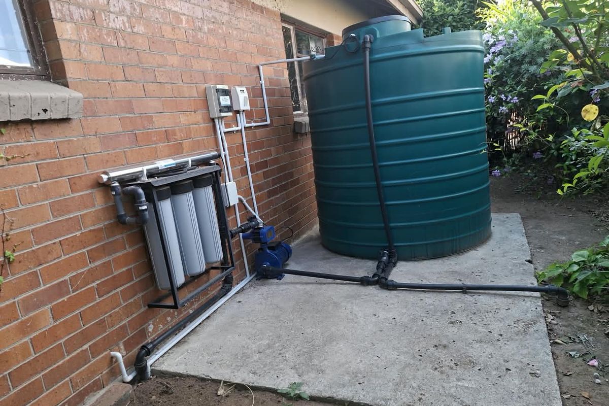 Exterior rear area featuring a water storage tank, pump, and filtration system installed on a concrete base against a brick wall.