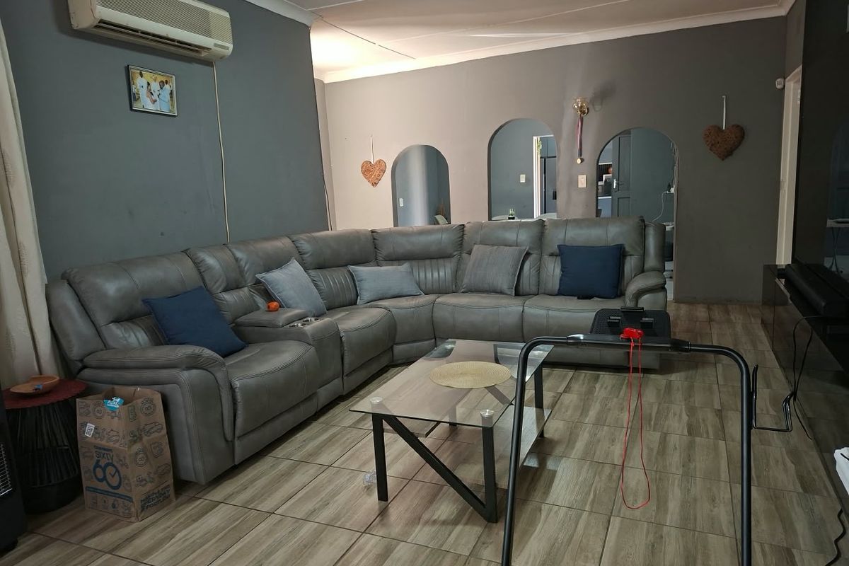 A living room featuring tiled flooring, arched doorways, and a wall-mounted air conditioning unit, offering a functional space with potential for cosmetic updates.