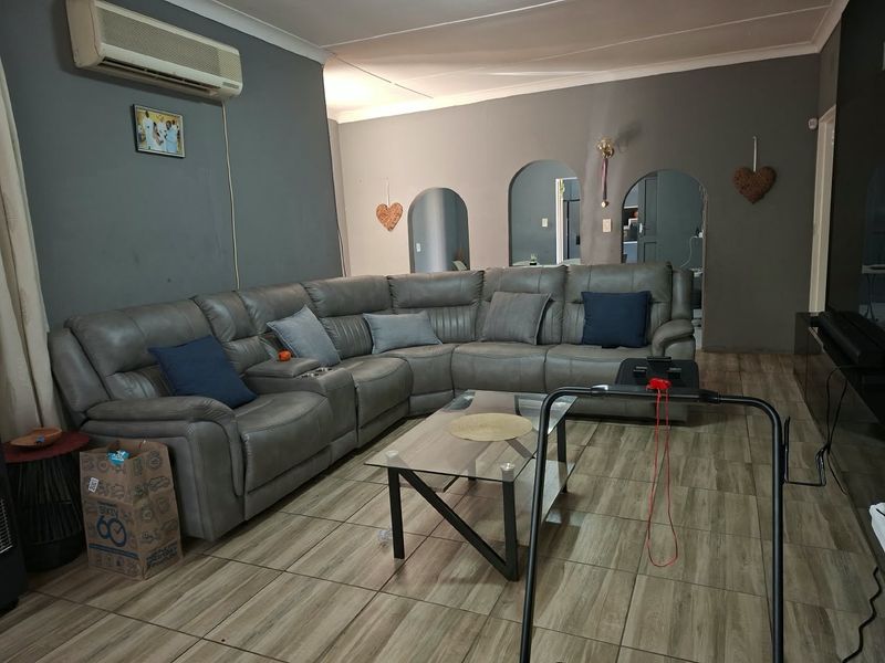 A living room featuring tiled flooring, arched doorways, and a wall-mounted air conditioning unit, offering a functional space with potential for cosmetic updates.