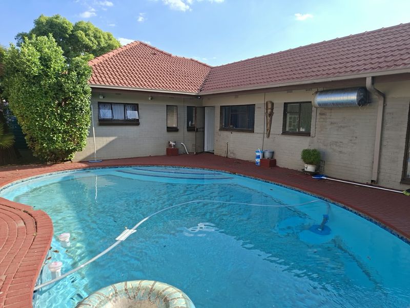 A backyard pool area featuring a swimming pool, brick paving, and a tiled roof structure with an external solar water heater.