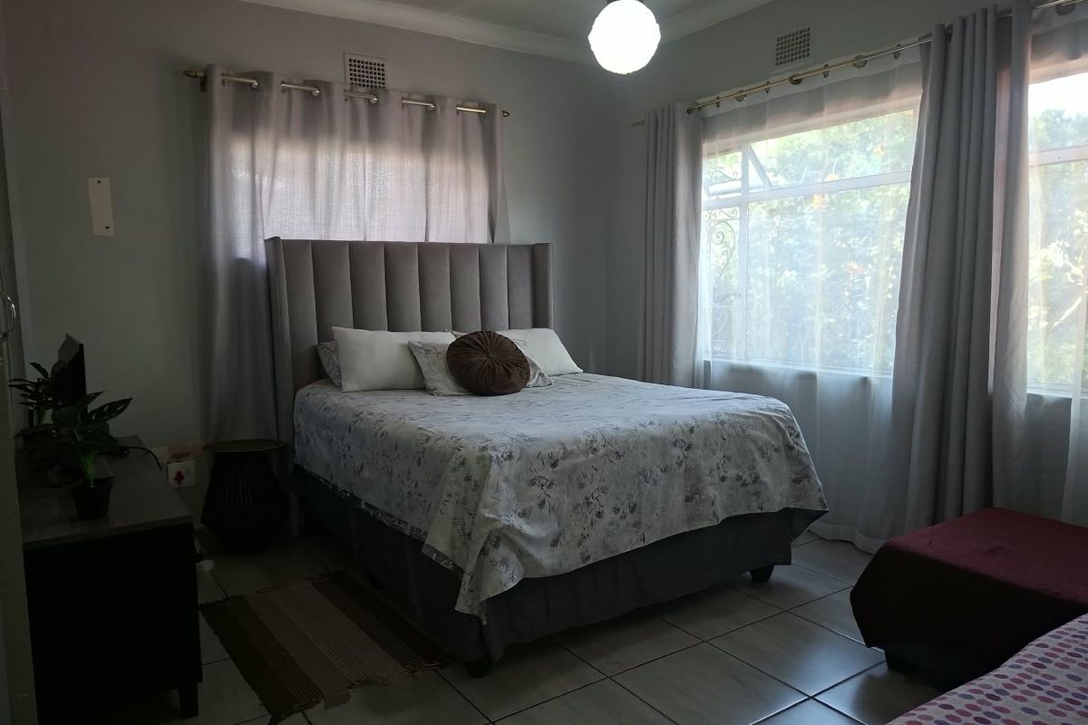 A bedroom featuring tiled flooring, ceiling cornices, and dual aspect windows with natural light.