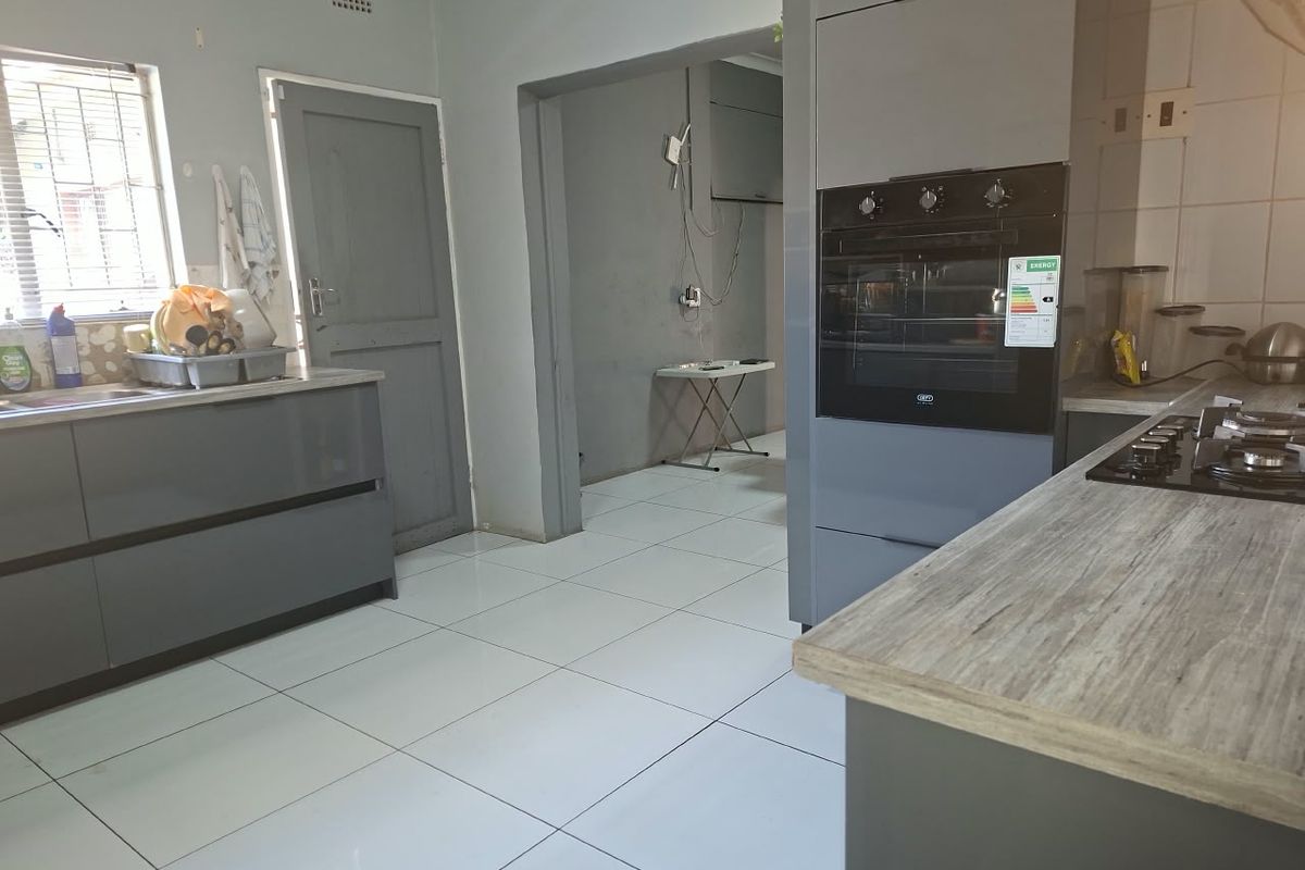 Modern grey kitchen featuring built-in oven, gas hob, laminate countertops, and tiled flooring, with an adjacent utility area visible through the doorway.