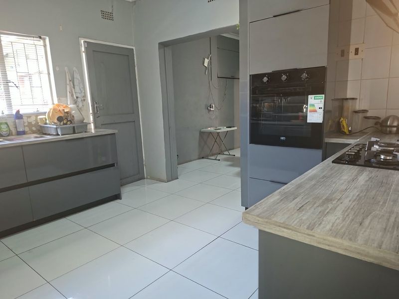 Modern grey kitchen featuring built-in oven, gas hob, laminate countertops, and tiled flooring, with an adjacent utility area visible through the doorway.