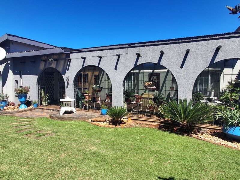 Rear exterior view of the house featuring a covered arched patio, paved flooring, and established garden landscaping.