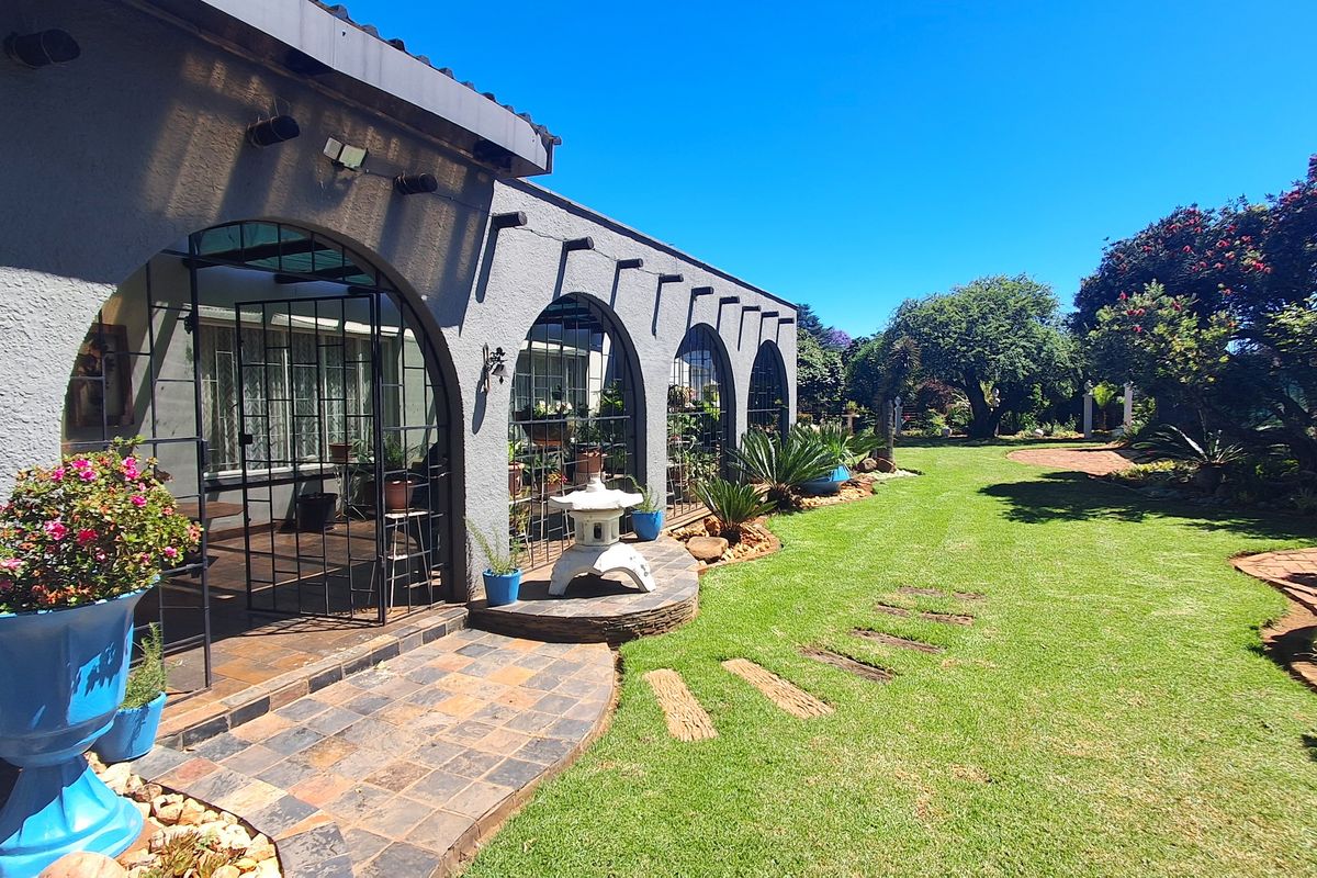 A well-maintained rear exterior featuring an arched covered patio with slate flooring, overlooking a lush, landscaped garden with mature trees and stone pathways.