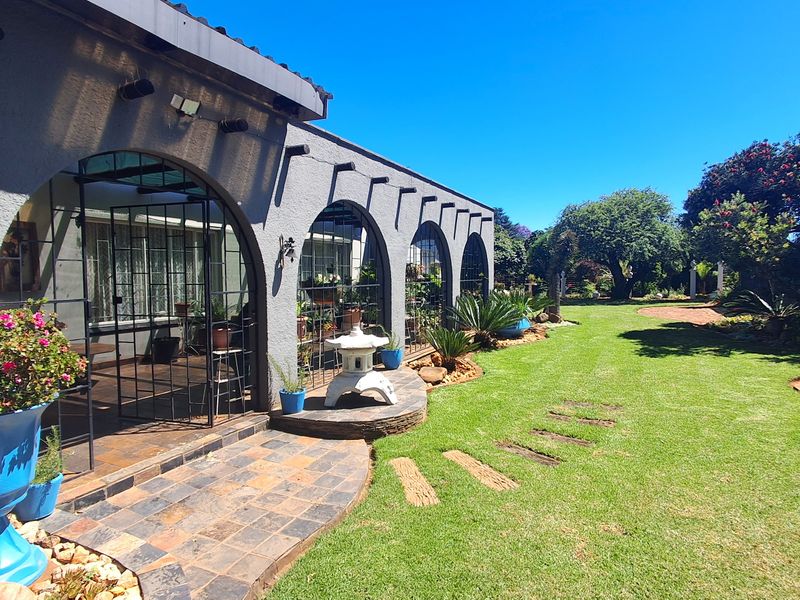 A well-maintained rear exterior featuring an arched covered patio with slate flooring, overlooking a lush, landscaped garden with mature trees and stone pathways.