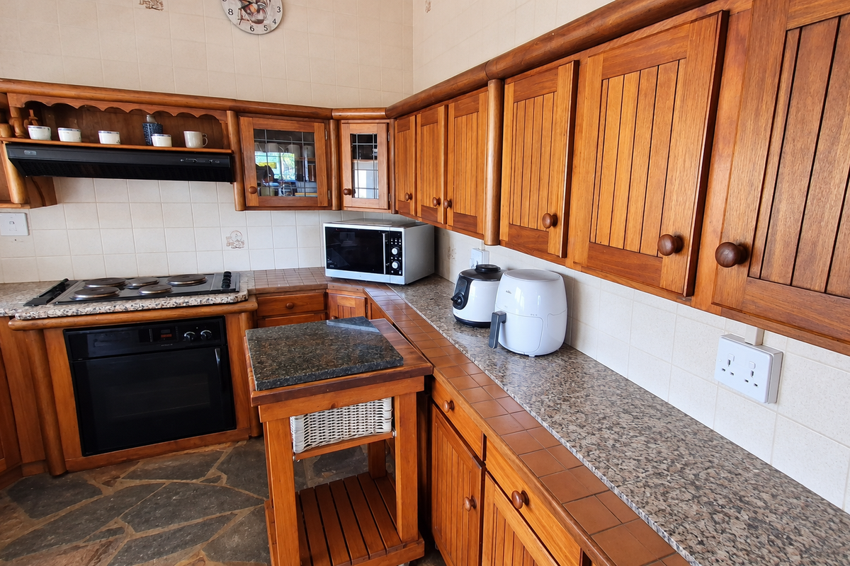 A traditional kitchen featuring solid wood cabinetry, granite countertops, built-in oven, electric hob, and durable stone flooring.