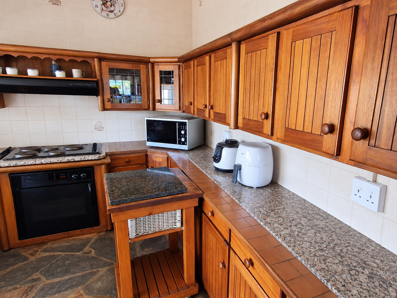A traditional kitchen featuring solid wood cabinetry, granite countertops, built-in oven, electric hob, and durable stone flooring.