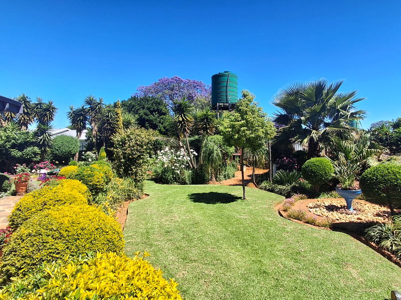 A well-maintained garden featuring a lush lawn, mature landscaping, and a prominent water tank, adjacent to a paved patio area.