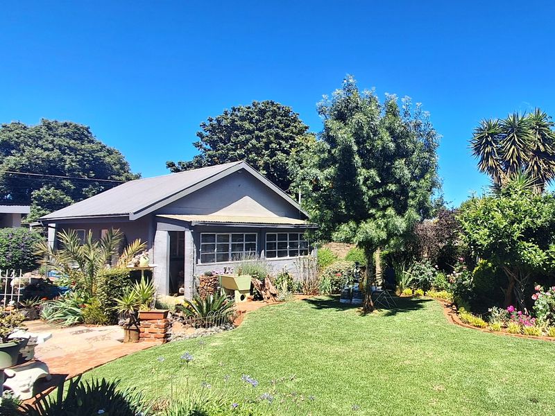 A well-maintained rear garden featuring a detached structure with a pitched metal roof and multi-pane windows, set within a landscaped outdoor area.