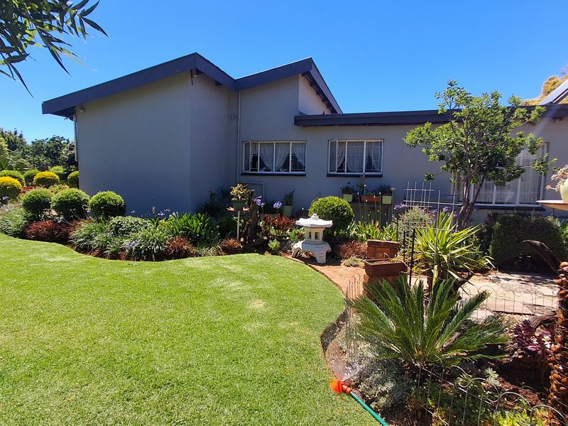 A well-maintained rear garden featuring a lush lawn, established landscaping, brick pathways, and a solar water heating system on the roof.