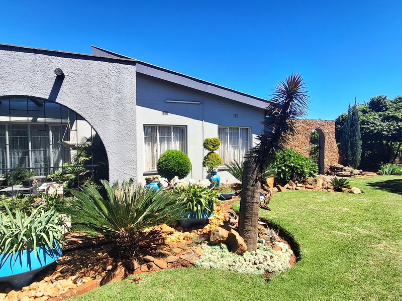 A well-maintained rear garden featuring a landscaped lawn, stone feature wall, and an arched patio area attached to the main house structure.