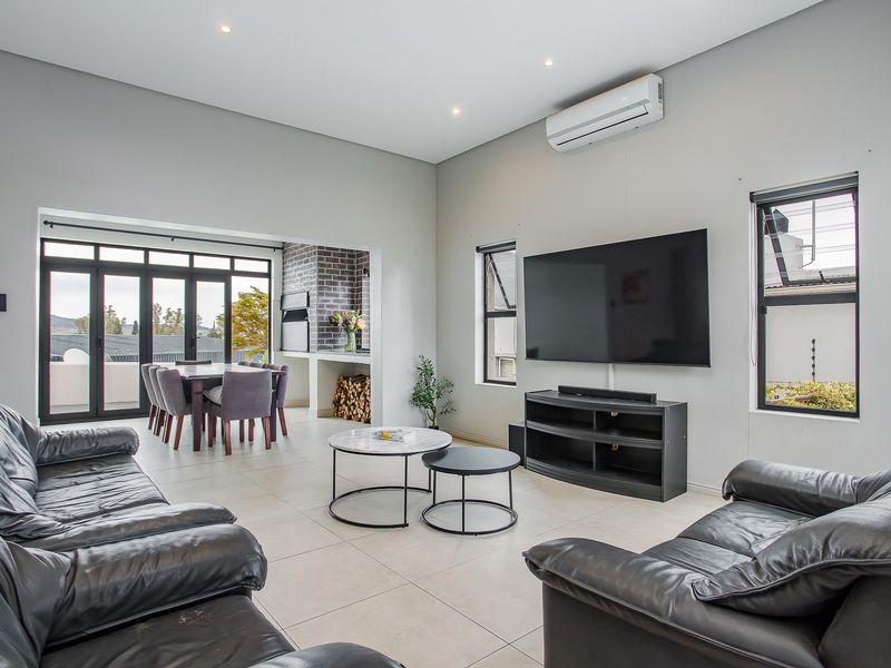 Spacious open-plan living and dining area featuring tiled floors, modern downlights, a built-in fireplace, and seamless access to the outdoor patio through stacker doors.