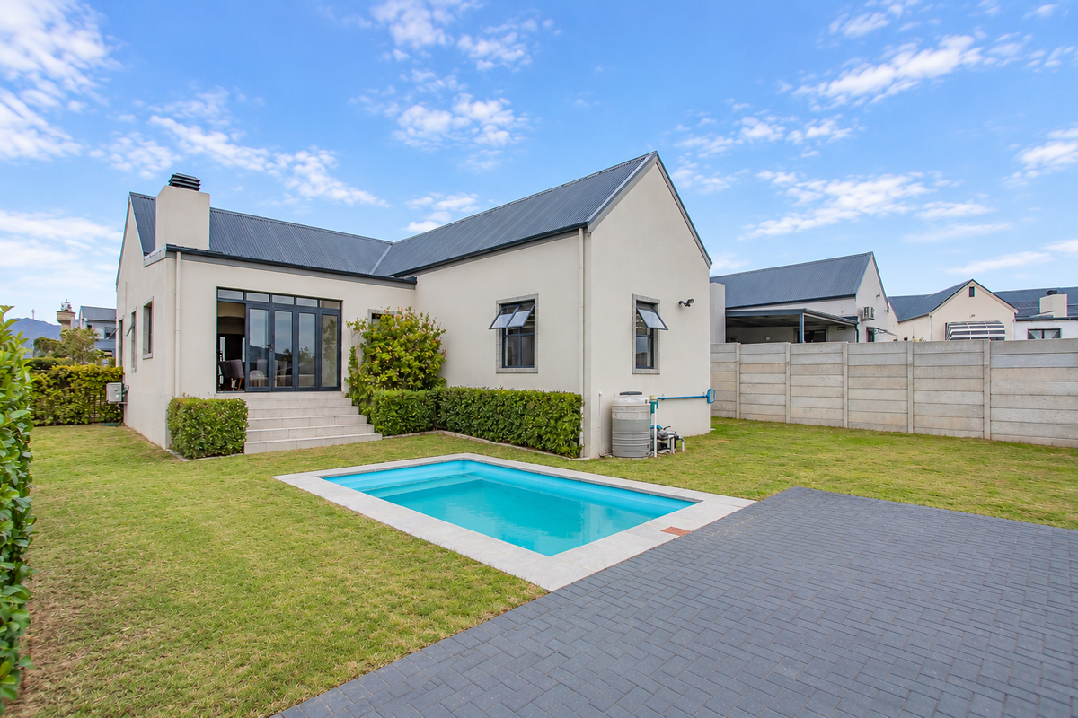 Rear view of the property featuring a swimming pool, paved patio area, well-maintained lawn, and a secure boundary wall.