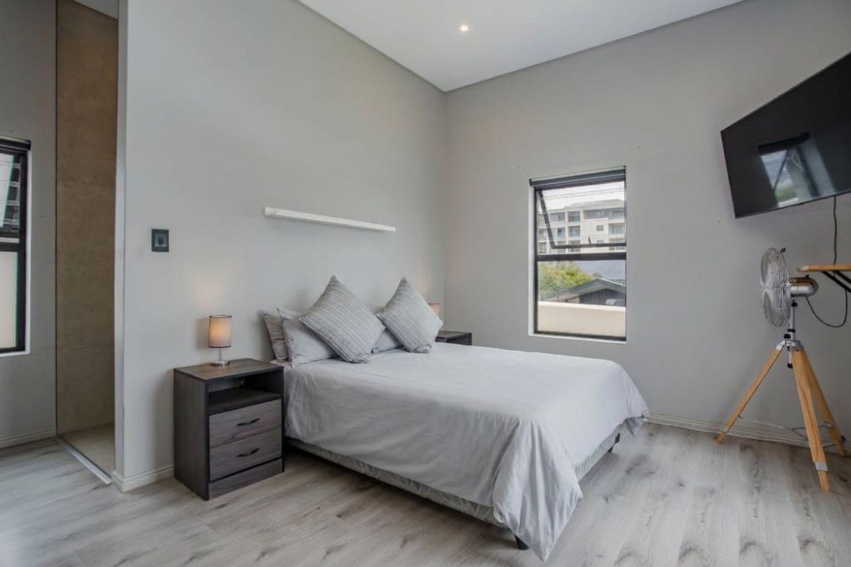 A modern, well-maintained bedroom featuring light-toned laminate flooring, neutral walls, and aluminium-framed windows.