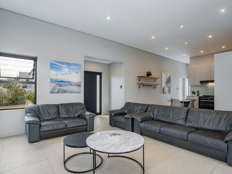 Spacious open-plan living area featuring modern tiled floors, recessed lighting, and a sleek kitchen with built-in appliances and subway tile backsplash.