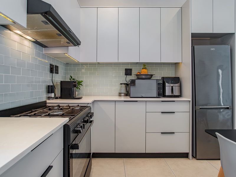 Modern kitchen featuring sleek white cabinetry, light blue subway tile backsplash, stone countertops, and a high-quality gas stove with an integrated extractor fan.