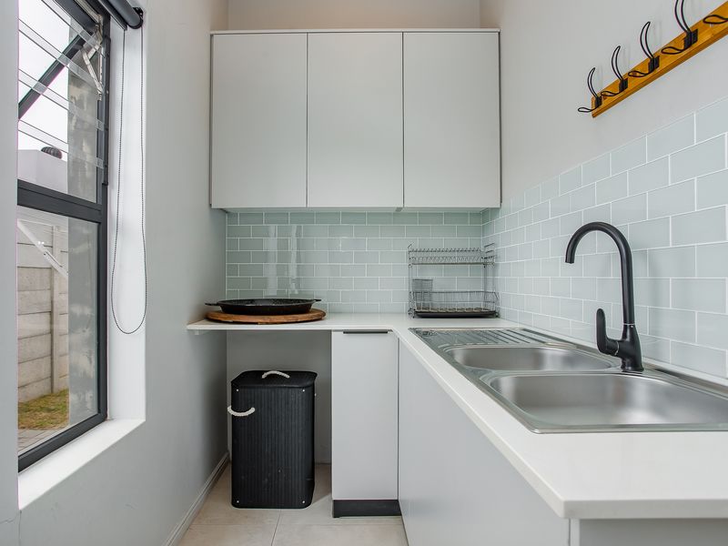 A clean and functional scullery featuring modern white cabinetry, a double stainless steel sink with a black mixer tap, and light blue subway tile backsplash.