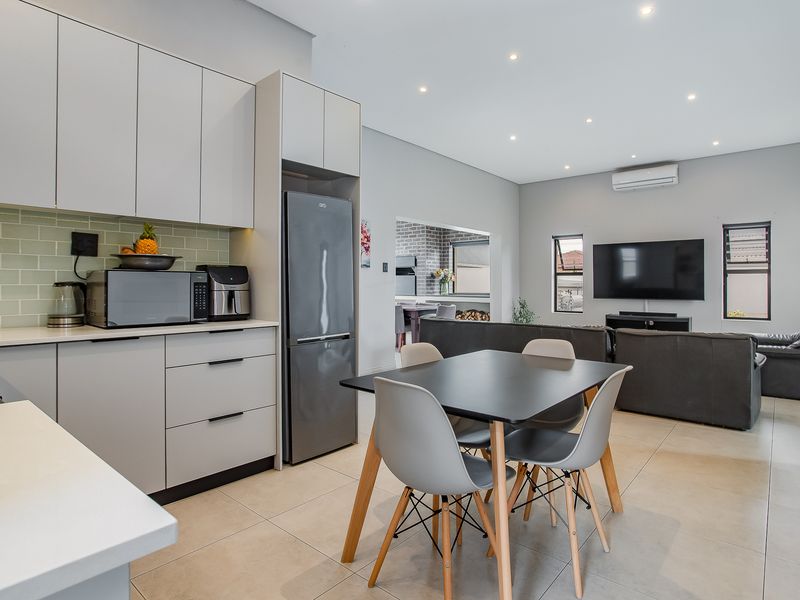 Modern open-plan living area featuring a sleek kitchen with subway tile backsplash, recessed lighting, and tiled flooring, seamlessly flowing into the lounge space.